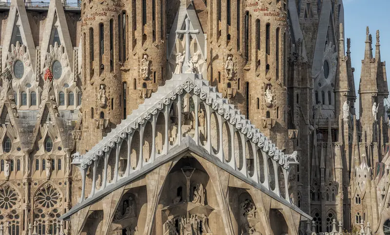 Bazylika Sagrada Familia przedstawiona w całej okazałości od strony wejścia, z tyłu widać żurawie używane przy budowie. / sagradafamilia.org