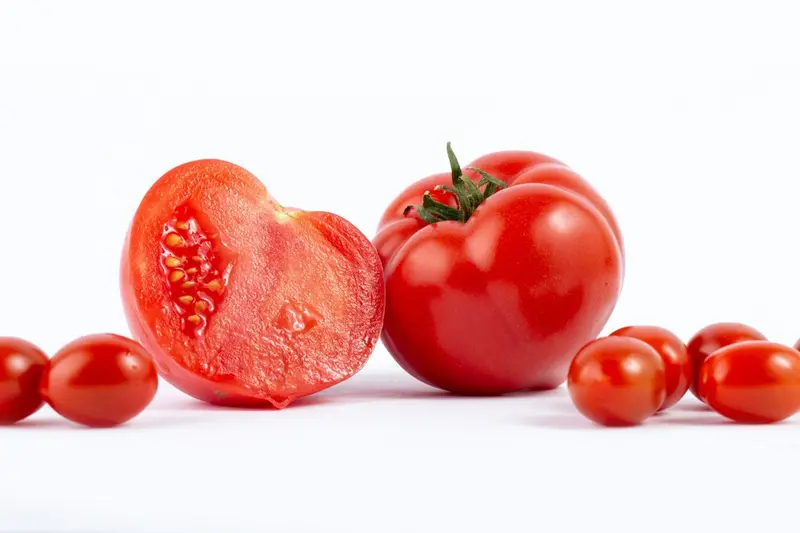 Zdjęcie całego i przekrojonego pomidora na pół, obok pomidorki cherry / fot. mdjaff freepik.com
